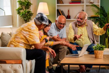 Ev içinde dizüstü bilgisayar kullanan kıdemli arkadaşlar rahat koltukta otururken Hintli Asyalı yaşlı erkekler ve kadınlar evlerinde kablosuz internet ile eğlenceli bir buluşma sırasında bilgisayarda bir şeyler planlıyorlar.