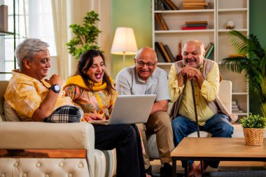 Ev içinde dizüstü bilgisayar kullanan kıdemli arkadaşlar rahat koltukta otururken Hintli Asyalı yaşlı erkekler ve kadınlar evlerinde kablosuz internet ile eğlenceli bir buluşma sırasında bilgisayarda bir şeyler planlıyorlar.