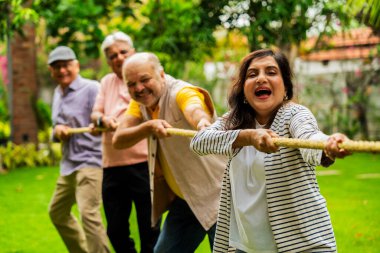 Bahçede çekiştirme oyunu oynayan son sınıf öğrencisi, Hintli Asyalı yaşlı arkadaşlar dışarıda halatla fiziksel aktivitenin keyfini çıkarıyorlar, gülüyorlar ve birlikte eğleniyorlar yeşil doğanın ortasında.