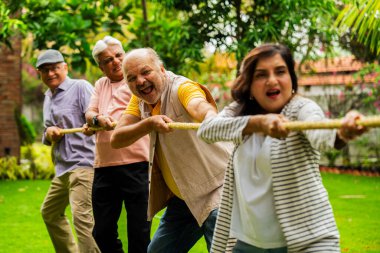 Bahçede çekiştirme oyunu oynayan son sınıf öğrencisi, Hintli Asyalı yaşlı arkadaşlar dışarıda halatla fiziksel aktivitenin keyfini çıkarıyorlar, gülüyorlar ve birlikte eğleniyorlar yeşil doğanın ortasında.