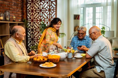 Son sınıflar birlikte yemek yiyor, Hintli Asyalı yaşlı arkadaşlar evde bir araya geliyor, yemek yiyor, atıştırmalık, soğuk içecek, çay ya da kahve servisi yapıyor, modern yemek masasında oturmuş, eğleniyorlar.