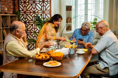 Son sınıflar birlikte yemek yiyor, Hintli Asyalı yaşlı arkadaşlar evde bir araya geliyor, yemek yiyor, atıştırmalık, soğuk içecek, çay ya da kahve servisi yapıyor, modern yemek masasında oturmuş, eğleniyorlar.
