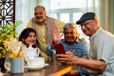Yemek masasında son sınıfların videosu, Hintli Asyalı yaşlıların evde buluşması, akıllı telefon kullanarak grup toplantısına katılması, modern kapalı yemek düzeninde çay, atıştırma ve arkadaşça sohbetler.