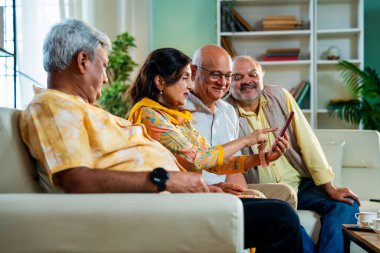 Hint Asya modern evindeki rahat koltukta otururken akıllı telefonları kontrol eden kıdemli arkadaşlar, rahat, neşeli ve mutlu bir şekilde cep telefonuyla buluşurken fotoğraflara bakıp gülüyorlar.