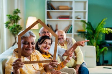 Son sınıflar koltukta otururken ev görüntülerini inceliyor, Hintli emekli arkadaşlar oturma odasında karton ev sembolü tutuyorlar yaşlılara ev bakımı ya da gayrimenkul konseptini desteklemek için.