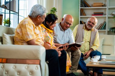 Son sınıflar rahat koltukta otururken fotoğraf albümüne bakarlar, Hintli Asyalı yaşlı arkadaşlar modern oturma odasında duygusal neşe ve sevinç içinde resimlere göz atarlar.