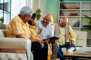 Son sınıflar rahat koltukta otururken fotoğraf albümüne bakarlar, Hintli Asyalı yaşlı arkadaşlar modern oturma odasında duygusal neşe ve sevinç içinde resimlere göz atarlar.