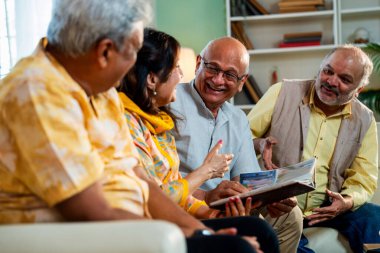 Son sınıflar rahat koltukta otururken fotoğraf albümüne bakarlar, Hintli Asyalı yaşlı arkadaşlar modern oturma odasında duygusal neşe ve sevinç içinde resimlere göz atarlar.