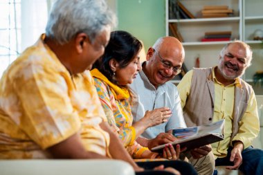 Son sınıflar rahat koltukta otururken fotoğraf albümüne bakarlar, Hintli Asyalı yaşlı arkadaşlar modern oturma odasında duygusal neşe ve sevinç içinde resimlere göz atarlar.