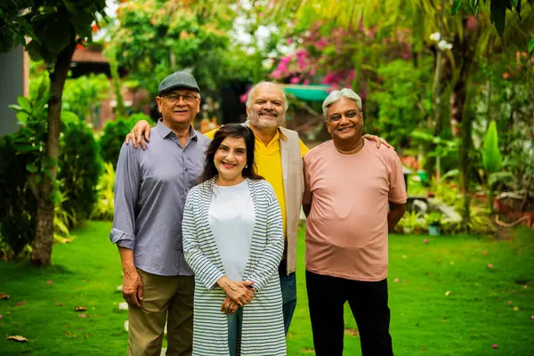 Hint kıdemli yetişkinler açık havada uyum içinde gülümsüyor, dört neşeli Asyalı yaşlı arkadaş grup halinde duruyorlar, mutluluk ve pozitiflik gösteriyorlar çiçeklerle dolu yemyeşil arka plana ve güneş ışığına karşı.