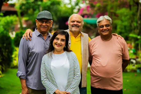 Hint kıdemli yetişkinler açık havada uyum içinde gülümsüyor, dört neşeli Asyalı yaşlı arkadaş grup halinde duruyorlar, mutluluk ve pozitiflik gösteriyorlar çiçeklerle dolu yemyeşil arka plana ve güneş ışığına karşı.