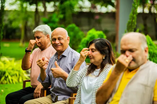 Hintli üst düzey arkadaşlar birlikte Pranayama ya da açık havada pranayam yapıyorlar, Asyalı yaşlılar bahçe ortamında nefes egzersizi yapıyorlar, kapalı gözlerle oturuyorlar, dikkatli yoga ve sağlığa odaklanıyorlar.