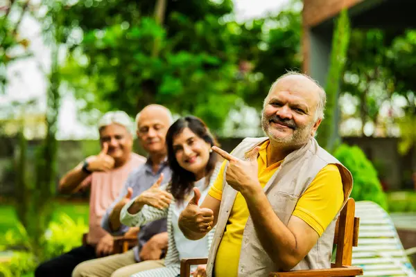 Hintli yaşlılar dışarıyı gösteriyor, Asyalı yaşlı arkadaşlar yemyeşil bahçe arka planına karşı sıralanmış, gülümsüyor ve kameraya bakarak olumlu ifadeler sergiliyorlar.