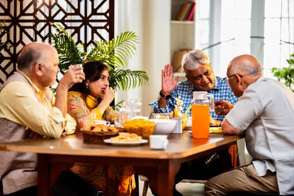 Son sınıflar yemek yerken sohbet ediyorlar, Hintli Asyalı yaşIı arkadaşlar yemek masasının etrafında neşeli sohbetler ve kahkahalar atarak evde atıştırmalık, çay, kahve ve yemek paylaşıyorlar.