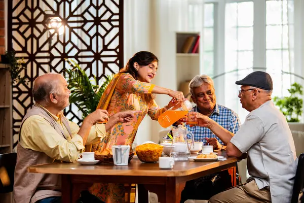 Son sınıflar birlikte yemek yiyor, Hintli Asyalı yaşlı arkadaşlar evde bir araya geliyor, yemek yiyor, atıştırmalık, soğuk içecek, çay ya da kahve servisi yapıyor, modern yemek masasında oturmuş, eğleniyorlar.