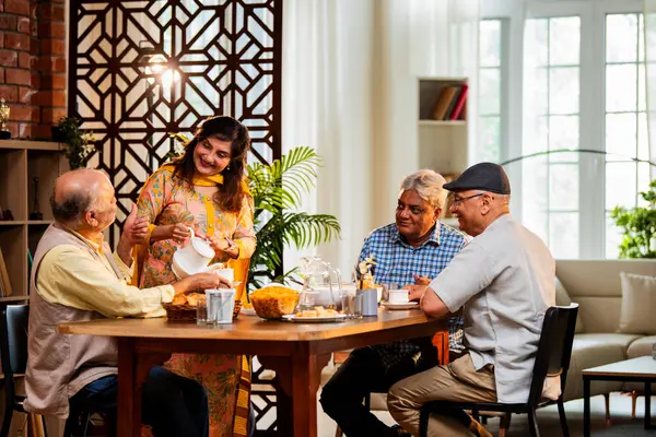 Son sınıflar birlikte yemek yiyor, Hintli Asyalı yaşlı arkadaşlar evde bir araya geliyor, yemek yiyor, atıştırmalık, soğuk içecek, çay ya da kahve servisi yapıyor, modern yemek masasında oturmuş, eğleniyorlar.