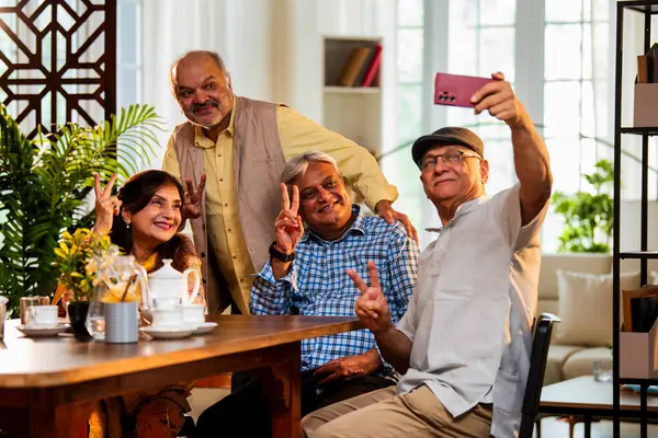 Son sınıflar yemek masasında selfie çekiyorlar, Hintli Asyalı yaşlı arkadaşlar evde buluşuyorlar, akıllı telefonla fotoğraf çektiriyorlar, modern yemek masasının etrafında çay, çay ve kahvenin tadını çıkarıyorlar.