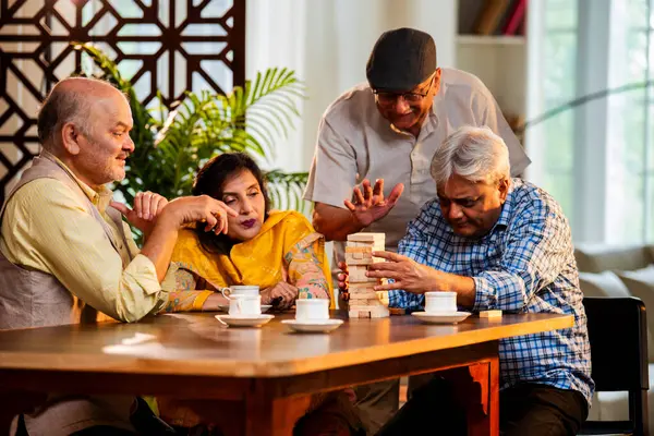 Hint kıdemli yetişkinler, Hint evinde yemek masasında oturmuş, gülüyor, eğlenceli anları kutluyor, kaynaşıyor, arkadaşça bir araya gelip eğleniyorlar.