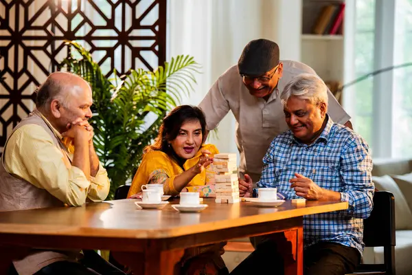 Hint kıdemli yetişkinler, Hint evinde yemek masasında oturmuş, gülüyor, eğlenceli anları kutluyor, kaynaşıyor, arkadaşça bir araya gelip eğleniyorlar.