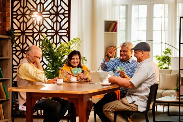 Hindistan 'daki son sınıf öğrencileri, rahat, modern bir evde yemek masasında oturmuş, neşeli bir şekilde gülüyor ve kaynaşıyorlar. Asyalı yaşlı arkadaşlar, kapalı alanda eğlenceli aktivitelerle neşeli bir buluşmayı kutluyorlar.