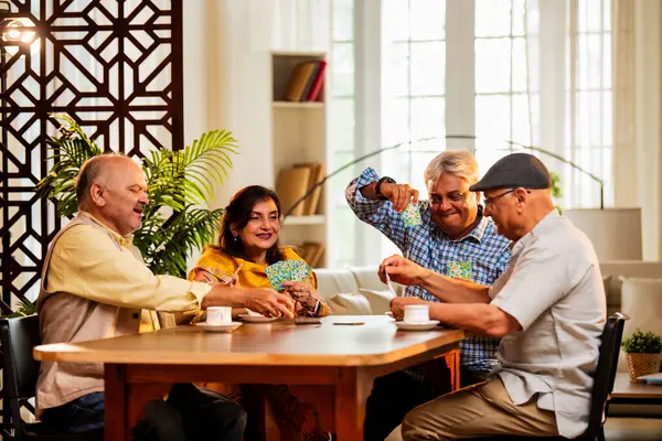Hindistan 'daki son sınıf öğrencileri, rahat, modern bir evde yemek masasında oturmuş, neşeli bir şekilde gülüyor ve kaynaşıyorlar. Asyalı yaşlı arkadaşlar, kapalı alanda eğlenceli aktivitelerle neşeli bir buluşmayı kutluyorlar.