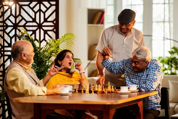 Hindistan 'daki son sınıf yetişkinler rahat bir evde yemek masasında oturmuş satranç oynarken gülümsüyor ve Shatranj maçının keyfini çıkarırken Asyalı eski dostlar kapalı alanda yeniden bir araya gelişlerini kutluyorlar.