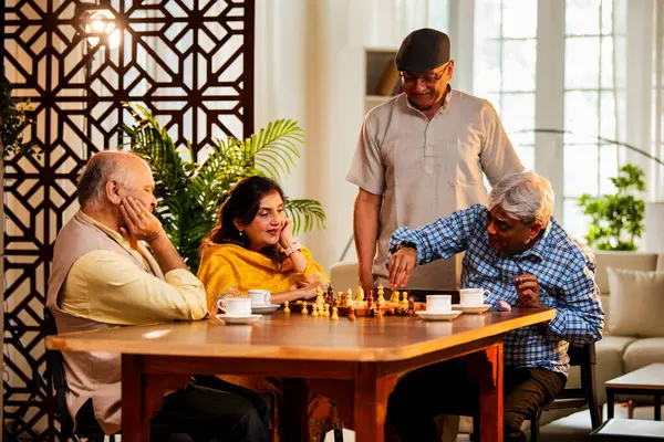 Hindistan 'daki son sınıf yetişkinler rahat bir evde yemek masasında oturmuş satranç oynarken gülümsüyor ve Shatranj maçının keyfini çıkarırken Asyalı eski dostlar kapalı alanda yeniden bir araya gelişlerini kutluyorlar.