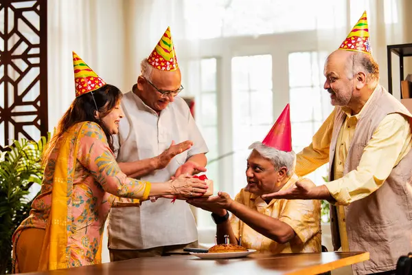 Hintli son sınıf arkadaşları evde doğum günü kutluyor, pasta kesiyor, kahkahalarla hediyeler alıyor, parti şapkaları takıyor, mumlarla çevrili, neşeli Asyalı yaşlılar toplanma kutlamasının keyfini çıkarıyorlar.