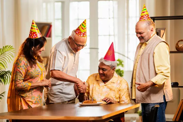 Hintli son sınıf arkadaşları evde doğum günü kutluyor, pasta kesiyor, kahkahalarla hediyeler alıyor, parti şapkaları takıyor, mumlarla çevrili, neşeli Asyalı yaşlılar toplanma kutlamasının keyfini çıkarıyorlar.