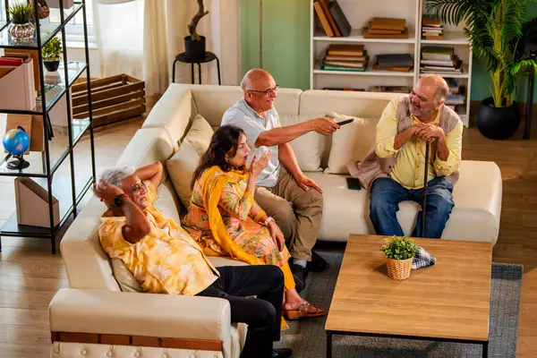 Hintli son sınıf öğrencisi rahat bir koltukta oturup televizyon izlerken gülerken Asyalı yaşlı erkekler ve kadınlar ellerinde uzaktan kumandayla televizyon izlerken televizyonda komik film ya da komedi şovu izliyorlar.