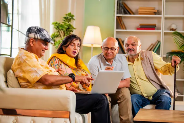 Ev içinde dizüstü bilgisayar kullanan kıdemli arkadaşlar rahat koltukta otururken Hintli Asyalı yaşlı erkekler ve kadınlar evlerinde kablosuz internet ile eğlenceli bir buluşma sırasında bilgisayarda bir şeyler planlıyorlar.