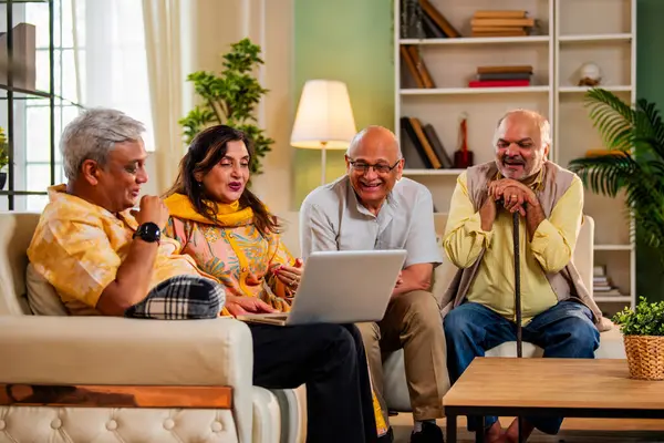 Ev içinde dizüstü bilgisayar kullanan kıdemli arkadaşlar rahat koltukta otururken Hintli Asyalı yaşlı erkekler ve kadınlar evlerinde kablosuz internet ile eğlenceli bir buluşma sırasında bilgisayarda bir şeyler planlıyorlar.