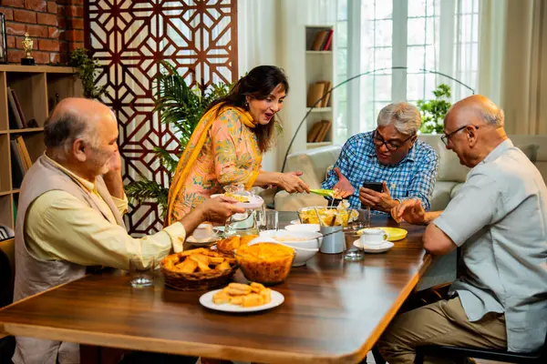 Son sınıflar birlikte yemek yiyor, Hintli Asyalı yaşlı arkadaşlar evde bir araya geliyor, yemek yiyor, atıştırmalık, soğuk içecek, çay ya da kahve servisi yapıyor, modern yemek masasında oturmuş, eğleniyorlar.