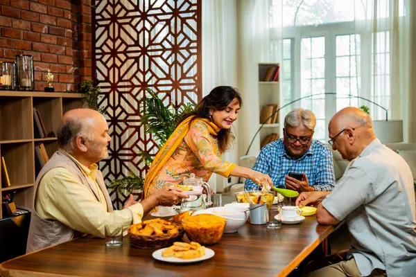 Son sınıflar birlikte yemek yiyor, Hintli Asyalı yaşlı arkadaşlar evde bir araya geliyor, yemek yiyor, atıştırmalık, soğuk içecek, çay ya da kahve servisi yapıyor, modern yemek masasında oturmuş, eğleniyorlar.