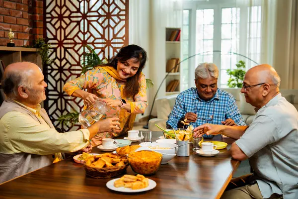Son sınıflar birlikte yemek yiyor, Hintli Asyalı yaşlı arkadaşlar evde bir araya geliyor, yemek yiyor, atıştırmalık, soğuk içecek, çay ya da kahve servisi yapıyor, modern yemek masasında oturmuş, eğleniyorlar.