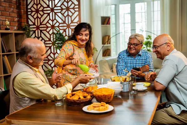 Son sınıflar birlikte yemek yiyor, Hintli Asyalı yaşlı arkadaşlar evde bir araya geliyor, yemek yiyor, atıştırmalık, soğuk içecek, çay ya da kahve servisi yapıyor, modern yemek masasında oturmuş, eğleniyorlar.