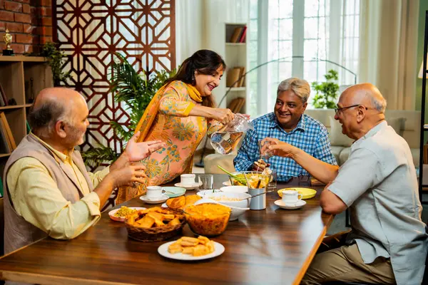 Son sınıflar birlikte yemek yiyor, Hintli Asyalı yaşlı arkadaşlar evde bir araya geliyor, yemek yiyor, atıştırmalık, soğuk içecek, çay ya da kahve servisi yapıyor, modern yemek masasında oturmuş, eğleniyorlar.