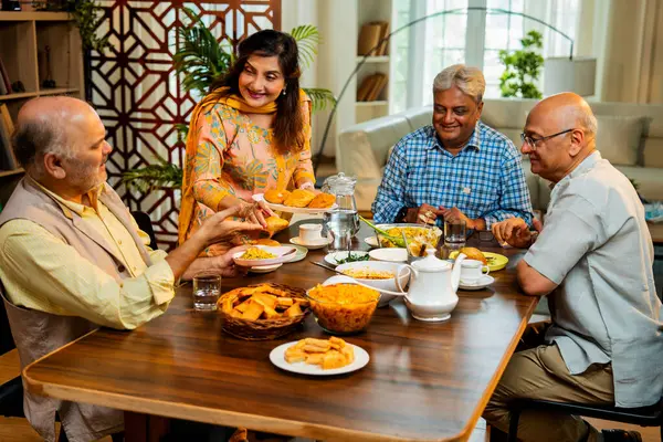 Son sınıflar birlikte yemek yiyor, Hintli Asyalı yaşlı arkadaşlar evde bir araya geliyor, yemek yiyor, atıştırmalık, soğuk içecek, çay ya da kahve servisi yapıyor, modern yemek masasında oturmuş, eğleniyorlar.