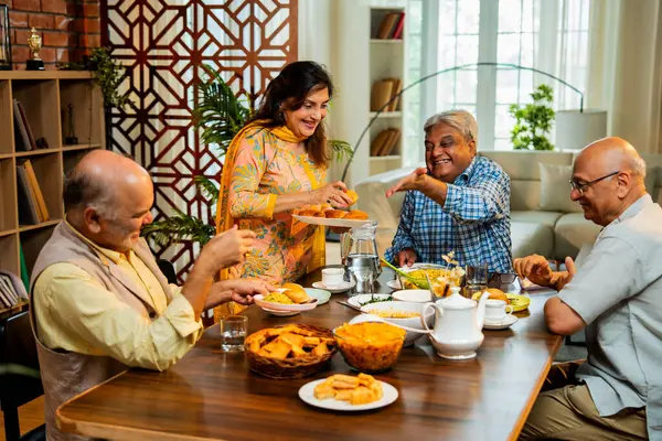 Son sınıflar birlikte yemek yiyor, Hintli Asyalı yaşlı arkadaşlar evde bir araya geliyor, yemek yiyor, atıştırmalık, soğuk içecek, çay ya da kahve servisi yapıyor, modern yemek masasında oturmuş, eğleniyorlar.