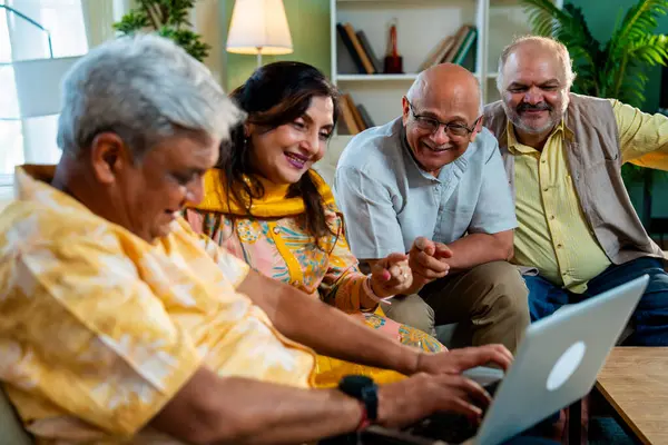 Ev içinde dizüstü bilgisayar kullanan kıdemli arkadaşlar rahat koltukta otururken Hintli Asyalı yaşlı erkekler ve kadınlar evlerinde kablosuz internet ile eğlenceli bir buluşma sırasında bilgisayarda bir şeyler planlıyorlar.