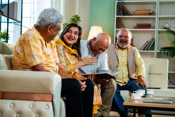 Son sınıflar rahat koltukta otururken fotoğraf albümüne bakarlar, Hintli Asyalı yaşlı arkadaşlar modern oturma odasında duygusal neşe ve sevinç içinde resimlere göz atarlar.