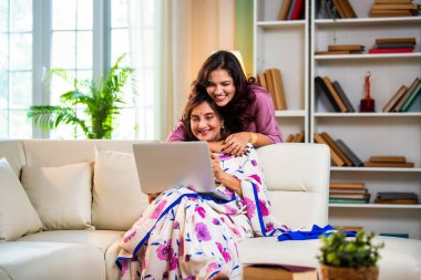 Yaşlı anne kız dizüstü bilgisayar kullanıyor, Hintli son sınıf öğrencisi sari giymiş genç kızı hem alışveriş yaparken, hem sörf yaparken, hem de modern evde kaliteli zaman geçirirken ekranda sarılıyor.