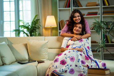 Hintli kıdemli anne kızı koltukta sarılıyor. Asyalı genç kız yaşlı anneye sürpriz yapıyor. Kitap okuyor, hem sohbet ediyor hem de modern oturma odasında mutlu bir bağ kuruyor.