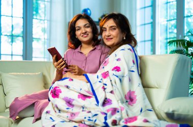 Yaşlı anne akıllı telefon kullanıyor, Hintli Asyalı yaşlı anne sari içinde genç kızıyla birlikte evde oturuyor, önemli bir şeyi tartışırken faiziyle telefon ekranına bakıyor.