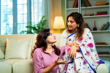 Yaşlı anne, kanepede otururken el ele tutuşarak sohbet ediyor. Hintli, Asyalı, sari giymiş yaşlı bir anne ve yanında oturan genç bir kız. Kapalı alanda samimi konuşmalar yapıyor.