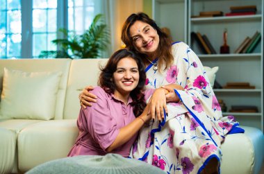 Yaşlı anne, kanepede otururken el ele tutuşarak sohbet ediyor. Hintli, Asyalı, sari giymiş yaşlı bir anne ve yanında oturan genç bir kız. Kapalı alanda samimi konuşmalar yapıyor.