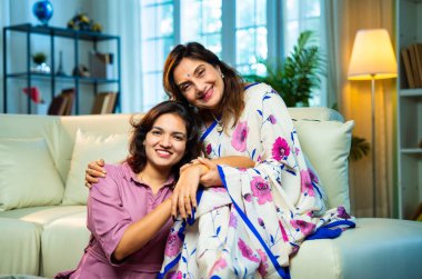 Yaşlı anne, kanepede otururken el ele tutuşarak sohbet ediyor. Hintli, Asyalı, sari giymiş yaşlı bir anne ve yanında oturan genç bir kız. Kapalı alanda samimi konuşmalar yapıyor.