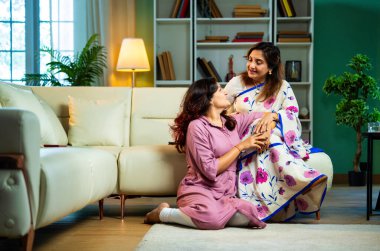 Yaşlı anne, kanepede otururken el ele tutuşarak sohbet ediyor. Hintli, Asyalı, sari giymiş yaşlı bir anne ve yanında oturan genç bir kız. Kapalı alanda samimi konuşmalar yapıyor.