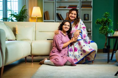 Yaşlı anne, kanepede otururken el ele tutuşarak sohbet ediyor. Hintli, Asyalı, sari giymiş yaşlı bir anne ve yanında oturan genç bir kız. Kapalı alanda samimi konuşmalar yapıyor.