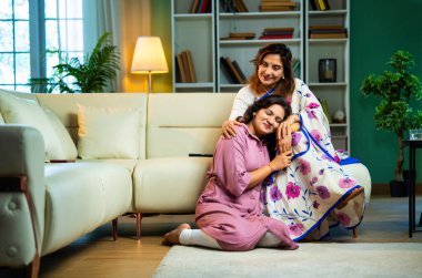 Yaşlı anne, kanepede otururken el ele tutuşarak sohbet ediyor. Hintli, Asyalı, sari giymiş yaşlı bir anne ve yanında oturan genç bir kız. Kapalı alanda samimi konuşmalar yapıyor.